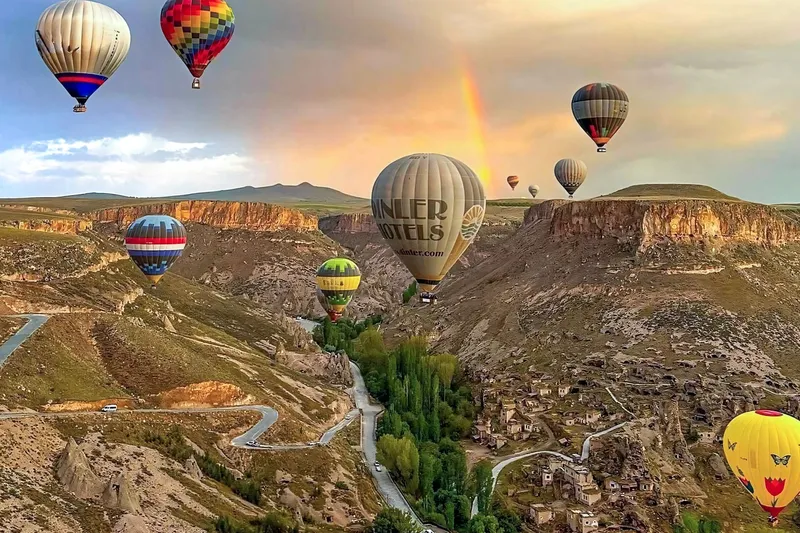 Heißluftballons über einem felsigen Tal unter einem Regenbogen